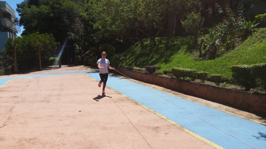 Usuária encontra-se na quadra de esportes, realizando atividade física de corrida, guiando-se por uma corda esticada, posicionada no decorrer do percurso na altura de sua cintura.